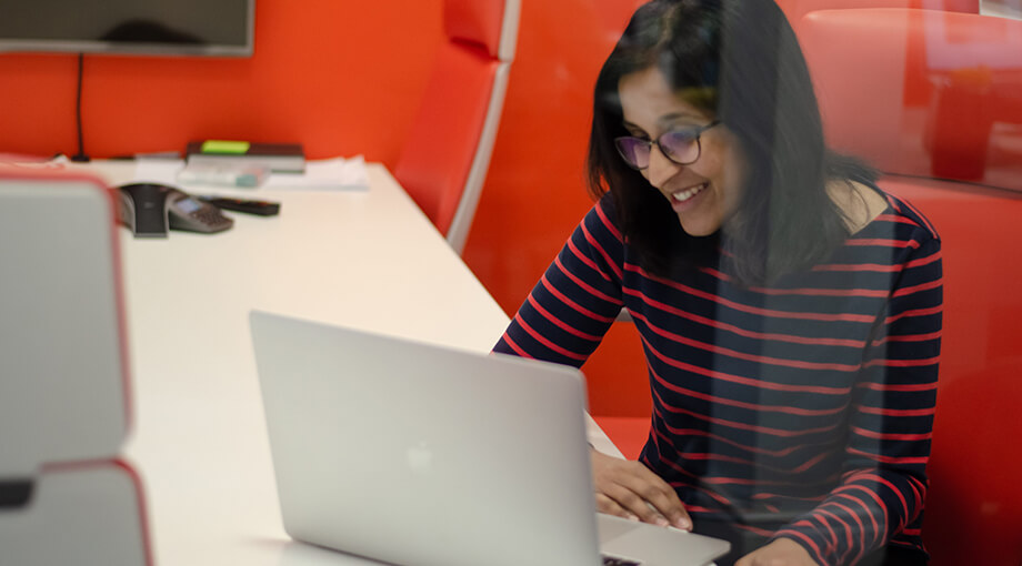 Photo of UX Designer Meera looking at her laptop whilst seated in Cyber-Duck's very orange office.