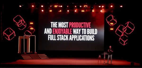 A picture of Taylor Otwell standing on a huge darkened stage at Laracon US 2024 in front of a slide in red and white Laravel brand colours that says: 'The most productive and enjoyable way to build full stack applications'