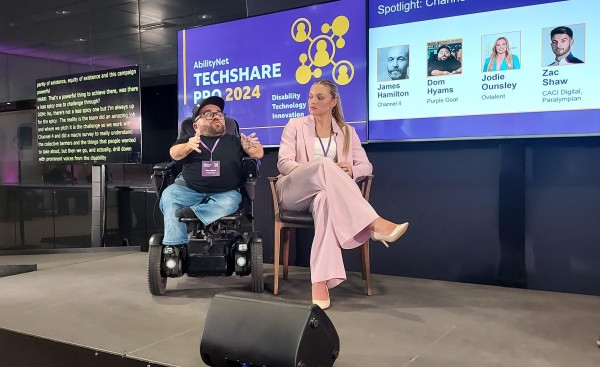 Dom Hyams, Global Client Director of Purple Goat Agency, who is a little person who uses a wheelchair for mobility, wearing a black baseball cap and T-shirt, sitting next to Jodie Ounsley, hearing impaired broadcaster, rugby player and TV Gladiator, wearing a pink suit  