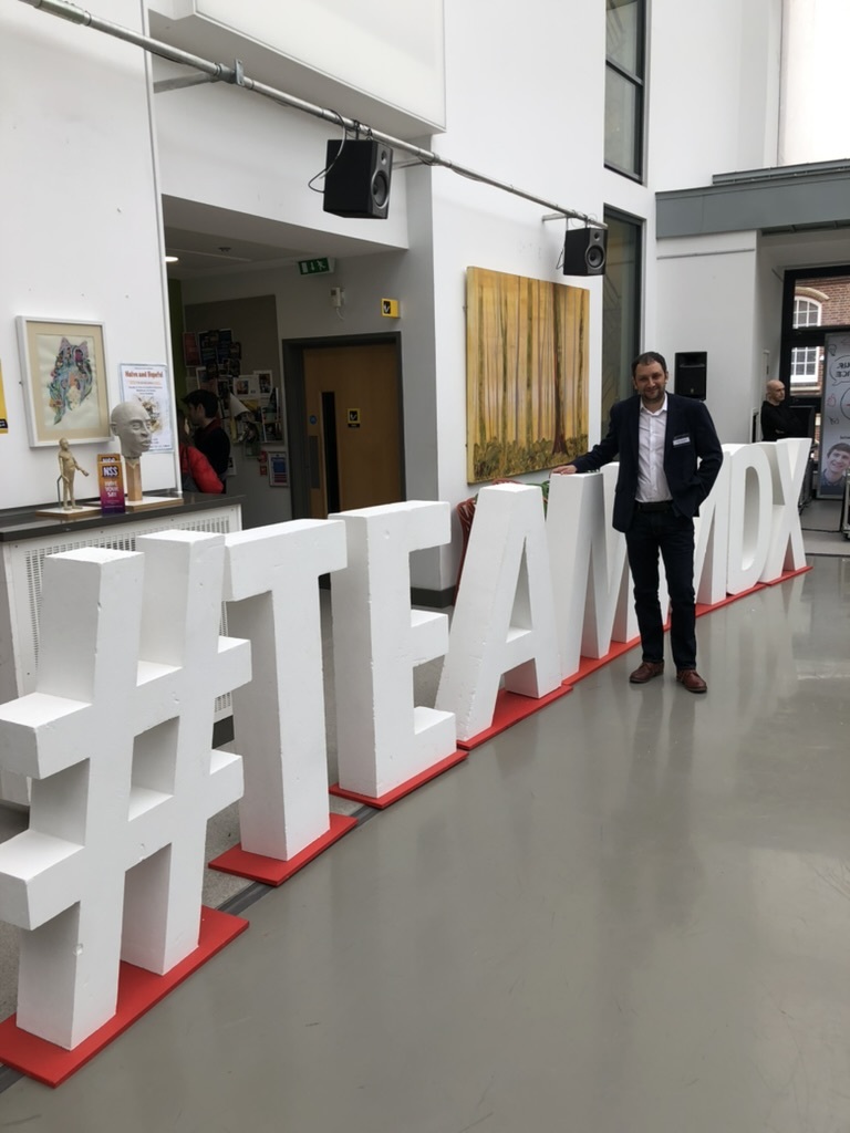 Danny indoors standing in front of a giant #TeamMDX sign at Middlesex University