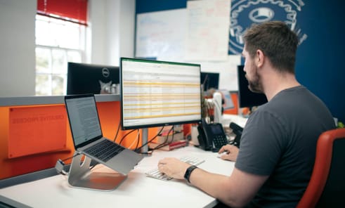 Photo of James at his desk looking at data on an Excel spreadsheet 